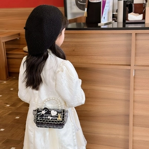 Girl wearing mini black and white tweed crossbody bag with pearl strap and bow detail