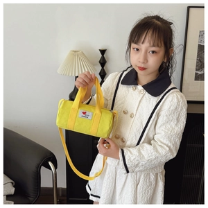 Detail of a bright yellow canvas bolster bag with heart patch shown on a child model