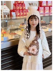 Close-up of a brown cartoon bear crossbody bag for kids in a cozy dessert shop setting