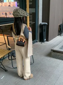 Dettaglio di una borsa a cilindro mini marrone scuro con manici in pelle chiara e tracolla