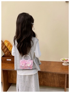 Girl wearing pink sequin crossbody bag with pearl handle and iridescent bow, back view