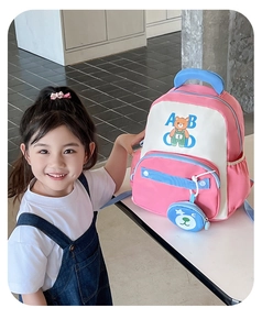 Detail view of pink and white bear backpack with side pocket and blue teddy pendant