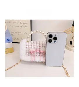 Sac à main rose à carreaux avec garniture peluche et perles montré à côté d'un smartphone