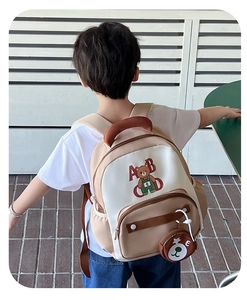 Outdoor shot showing a child wearing the beige bear backpack with a matching mini pouch