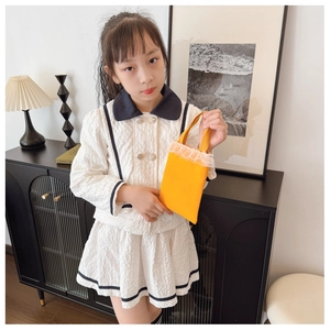 Close-up of children's cream dress with textured fabric and yellow lace handbag detail