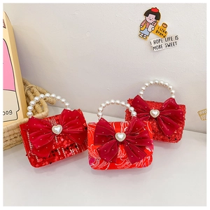 Detail of red festive kids' handbags featuring velvet bows and pearl handles