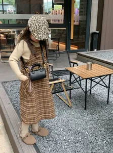 Bambina con basco leopardato e abito a quadri con una mini borsa in pelle nera