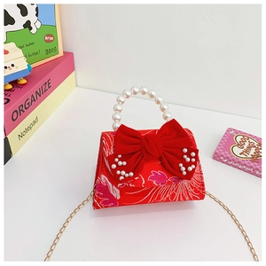 Detail of red girl's handbag with large velvet bow, pearl handle and gold chain strap