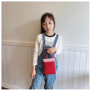 Detail of red canvas mini handbag for girls featuring delicate white lace trim and handles
