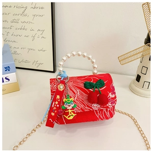 Close-up of red festive kids bag with pearl handle, cherry decor, and gold chain strap