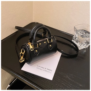Dettaglio macro della pelle nera a grana e hardware dorato della mini borsa a bauletto
