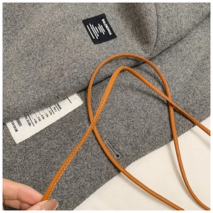 Detail shot of luxury brand logo on a grey wool bag with an orange leather strap