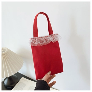Detail of red canvas girl's handbag featuring white lace trim and ribbon handles
