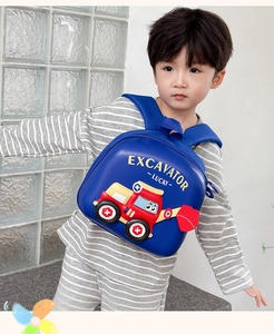 Blue toddler backpack with 3D cartoon excavator worn by a child against a glass brick wall