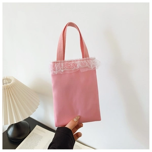Detail of pink girls handbag with white lace trim and woven handles in a bright setting