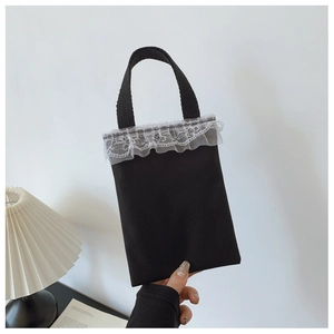 Detail of black canvas handbag with white lace trim and minimalist top handle design