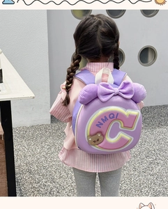 Back view of girl wearing purple child backpack with large plush bow and bear badge