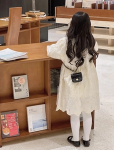 Detailed view of child wearing lace dress with black quilted mini bag and floral clasp