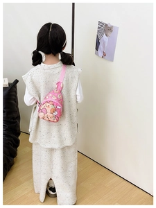 Rear view of a pink cartoon bear crossbody chest bag worn by a child in a home setting