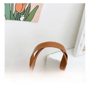 Détail de la texture en cuir marron et des coutures sur la poignée du sac panier pour enfant