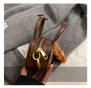Detail of dark brown mini bag featuring gold zipper and brown plush bear charm