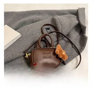 Detail view of brown leather crossbody bag with letter embossing and plush bear charm