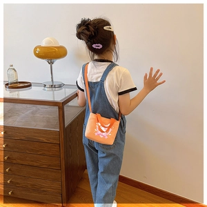 Toddler modeling orange canvas crossbody bag with cute heart and bow print in a home setting
