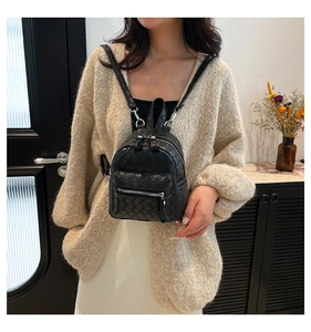 Detail of a black quilted mini backpack featuring silver hardware worn by a model indoors