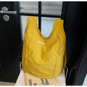 Close-up of ginger yellow nylon tote bag featuring white FASHION text in detail
