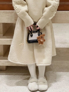 Detail of girl's shell bag featuring cream fabric, black leather trim and plush bear charm