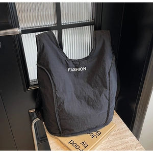 Detail of black quilted nylon tote bag featuring white FASHION text and wide shoulder strap