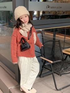 Détail d'un cardigan en maille rouge à boutons en bois et d'un mini sac matelassé enfant