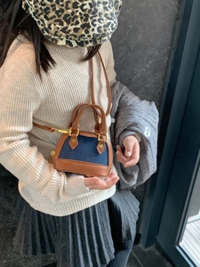 Toddler girl modeling a mini denim and brown leather shell bag with gold hardware