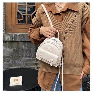 Nahaufnahme des cremefarbenen Mini-Lederrucksacks mit geprägtem Logo und Klappentaschen