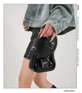 Detail of glossy black patent leather crescent bag with a silver metal bow accent