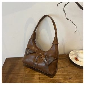 Detail of vintage brown shoulder bag with plaid pattern and bow accent on wooden table
