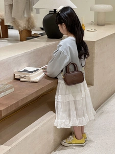 Girl wearing a brown mini bowling bag with embossed letters and metal strap hooks