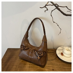 Close-up of brown faux leather shoulder bag featuring leopard print bow and vintage buttons