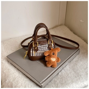 Detail of checkered shell bag with brown leather trim and a cute plush bear pendant