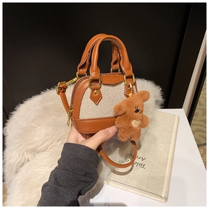 Detail of canvas shell bag with brown leather trim and a cute plush bear charm