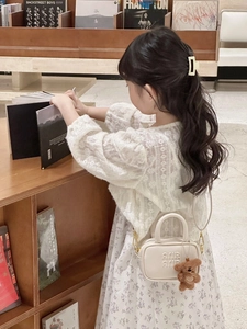 Toddler girl carrying cream handbag with letter embossing and plush bear charm