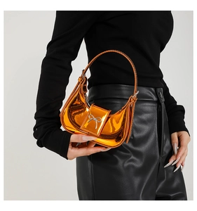 Detail of glossy orange moon bag featuring a silver metallic bow and slim handle strap