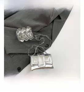 Detail of silver mirror patent leather mini bag with fine metal chain strap on gray suit