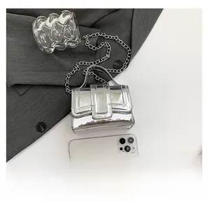 Mini silver mirror chain bag with metallic handle next to a phone for size reference