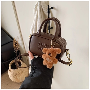 Detail of a mini brown leather tote with embossed letters and a cute plush bear charm