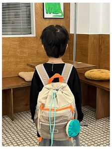 Rear view of child wearing beige drawstring backpack with blue cords and mini pouch