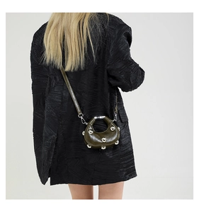 Detail of dark olive crescent bag with silver studs worn with a black pleated blazer
