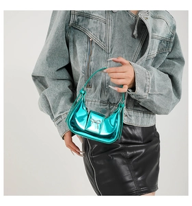 Close-up of metallic teal crescent handbag with silver bow detail held by a model