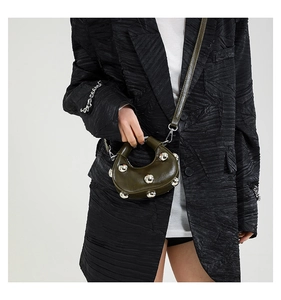 Macro detail of dark green glossy leather handbag featuring silver metallic stud accents