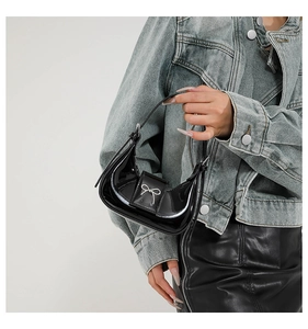 Detail of black patent leather crescent bag with a silver metal bow accent
